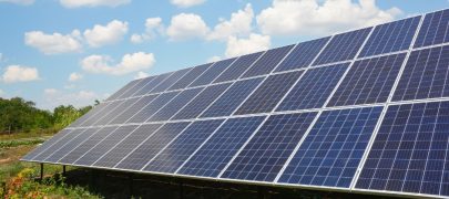 Ground-mounted commercial energy solar panels in green fields and surrounded by blue skies and fluffy white clouds